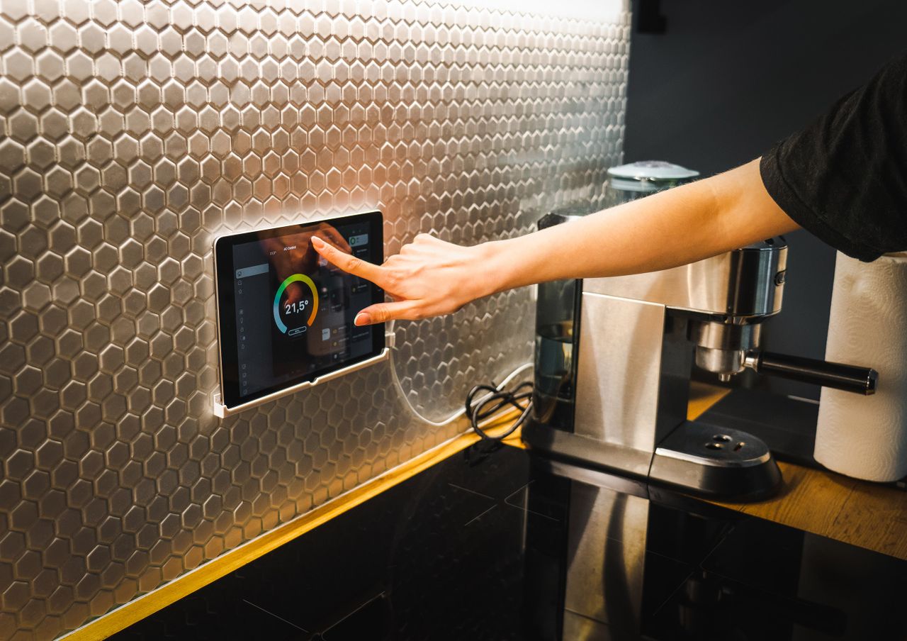 services-04 Modern kitchen scene featuring a hand using a tablet to control a smart home system.